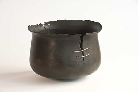 Burnt wooden vessel with cracked rim, repaired with hand-beaten copper wire