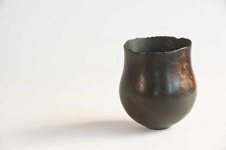 Burnt wooden vessel with chard rim, repaired with hand-beaten copper