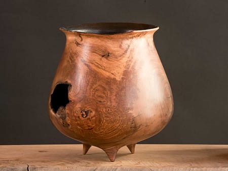 Blackened wooden vessel with broken rim and large hole in side, resembling a scorched cauldron.